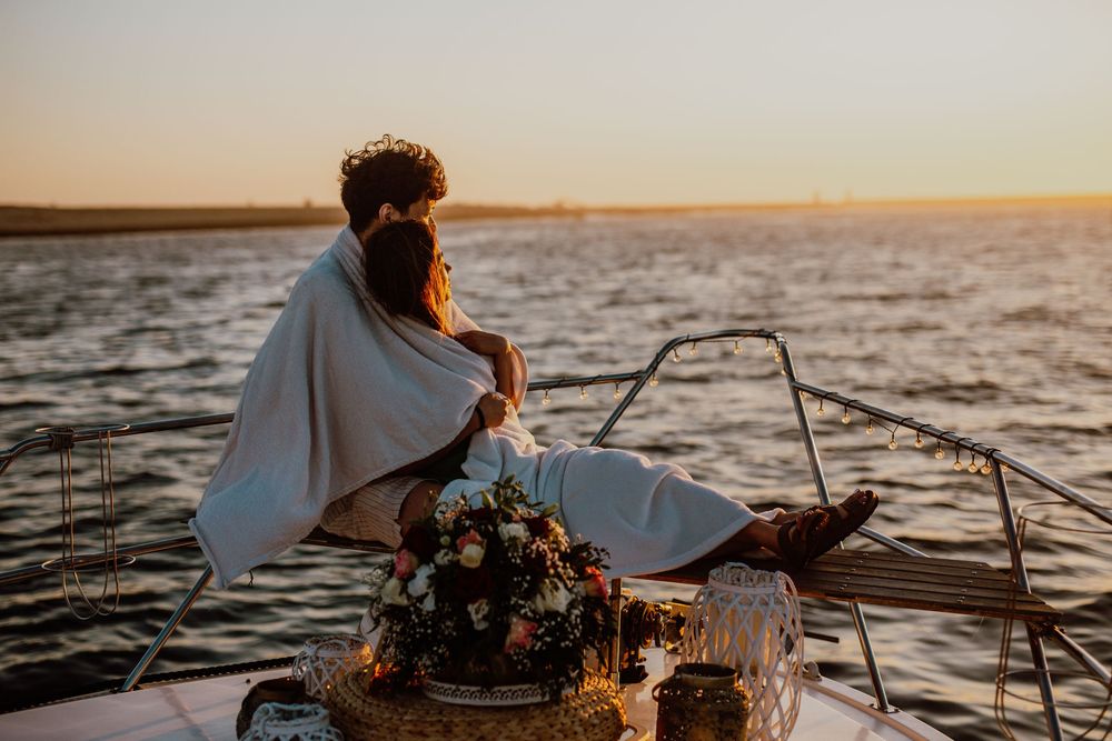 A silhouetted figure steers a boat across calm waters during a golden sunset on the horizon.