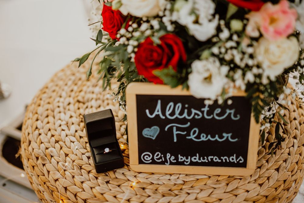 A small chalkboard sign with social media handle sits on a woven rattan charger with red and white floral arrangements.