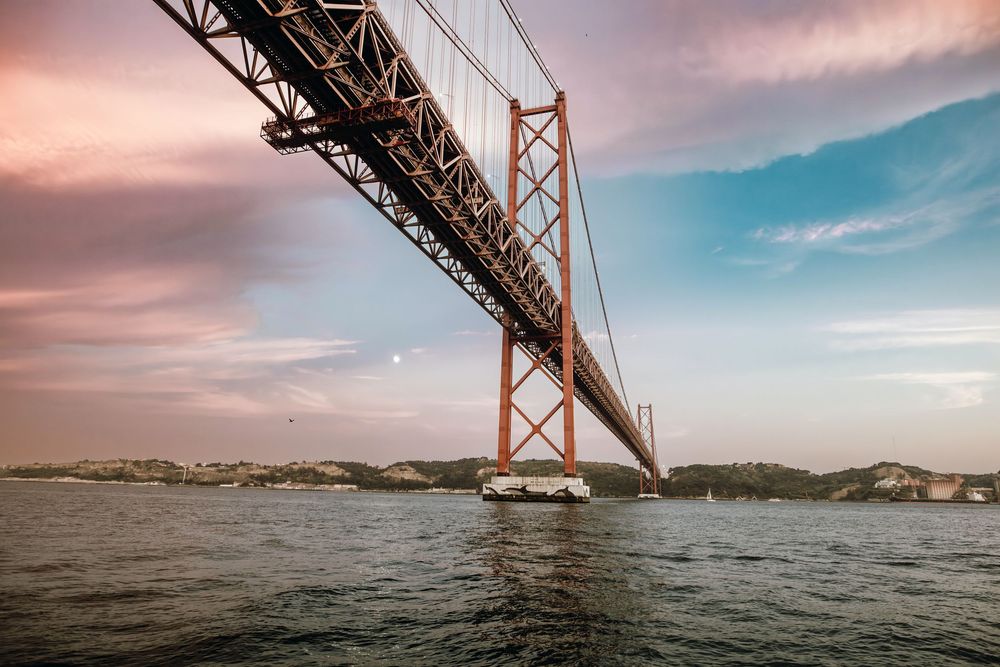 Panoramic view of the iconic Golden Gate Bridge at sunset with dramatic pink and orange sky over San Francisco Bay.