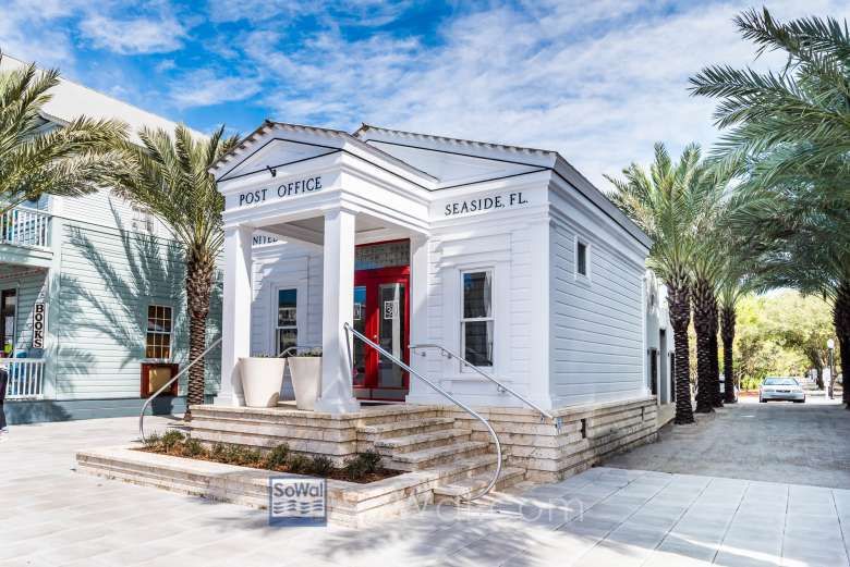 A panoramic view of coastal buildings and palm trees along a beachfront street with red umbrellas and pedestrians.