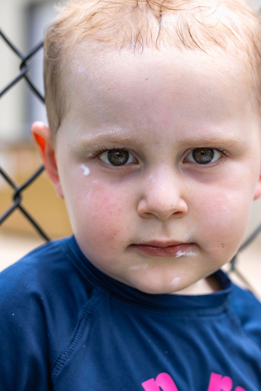 Close-up sequence of a baby with bright eyes wearing a navy blue shirt against a chain link fence background.