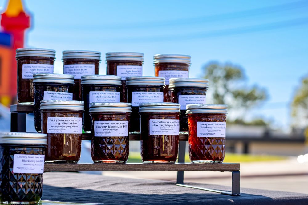 Rows of glass jars filled with homemade jam or preserves lined up on wooden shelves in sunlight.