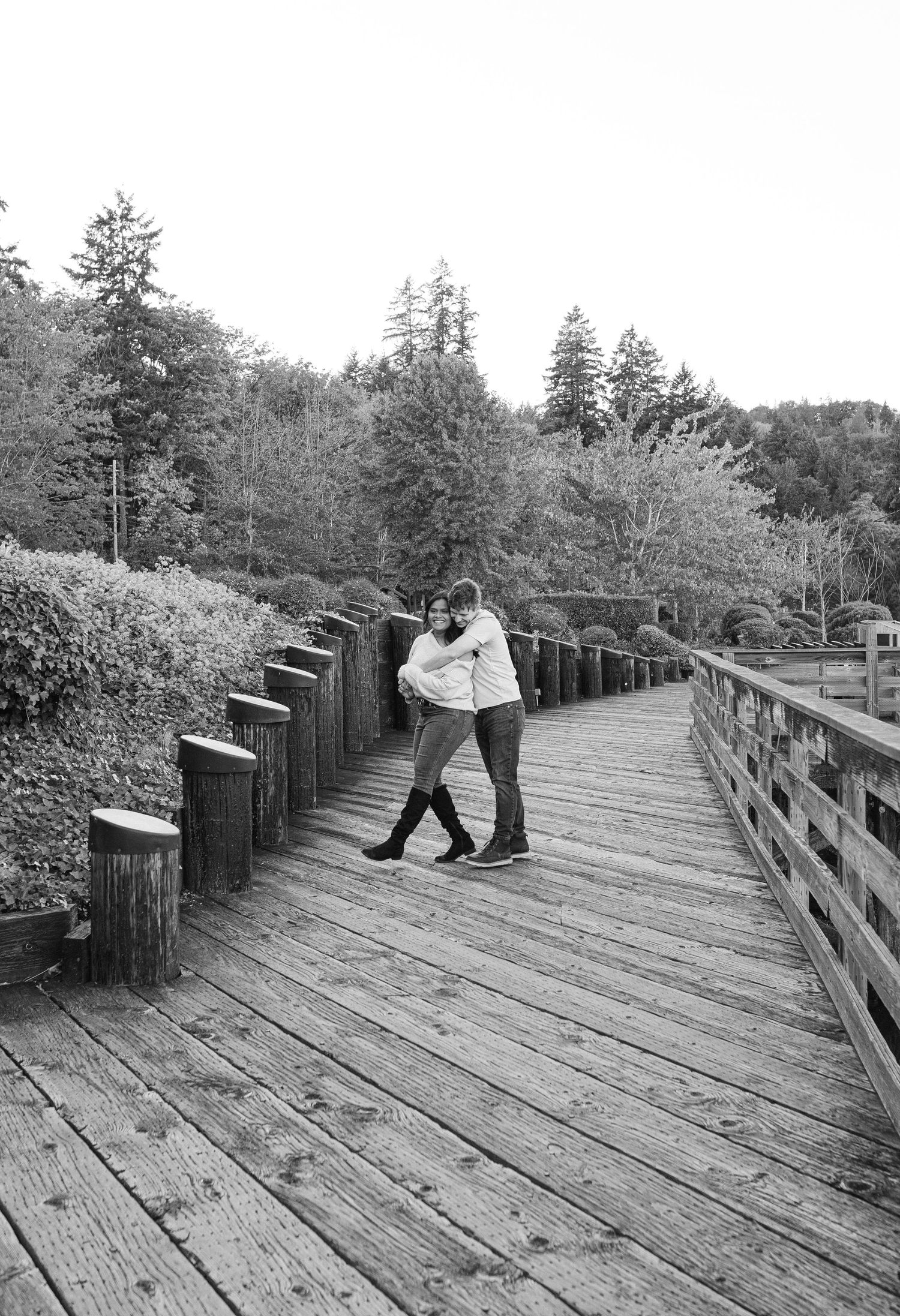 A sequence of black and white photos showing a couple dancing playfully on a wooden boardwalk surrounded by trees.