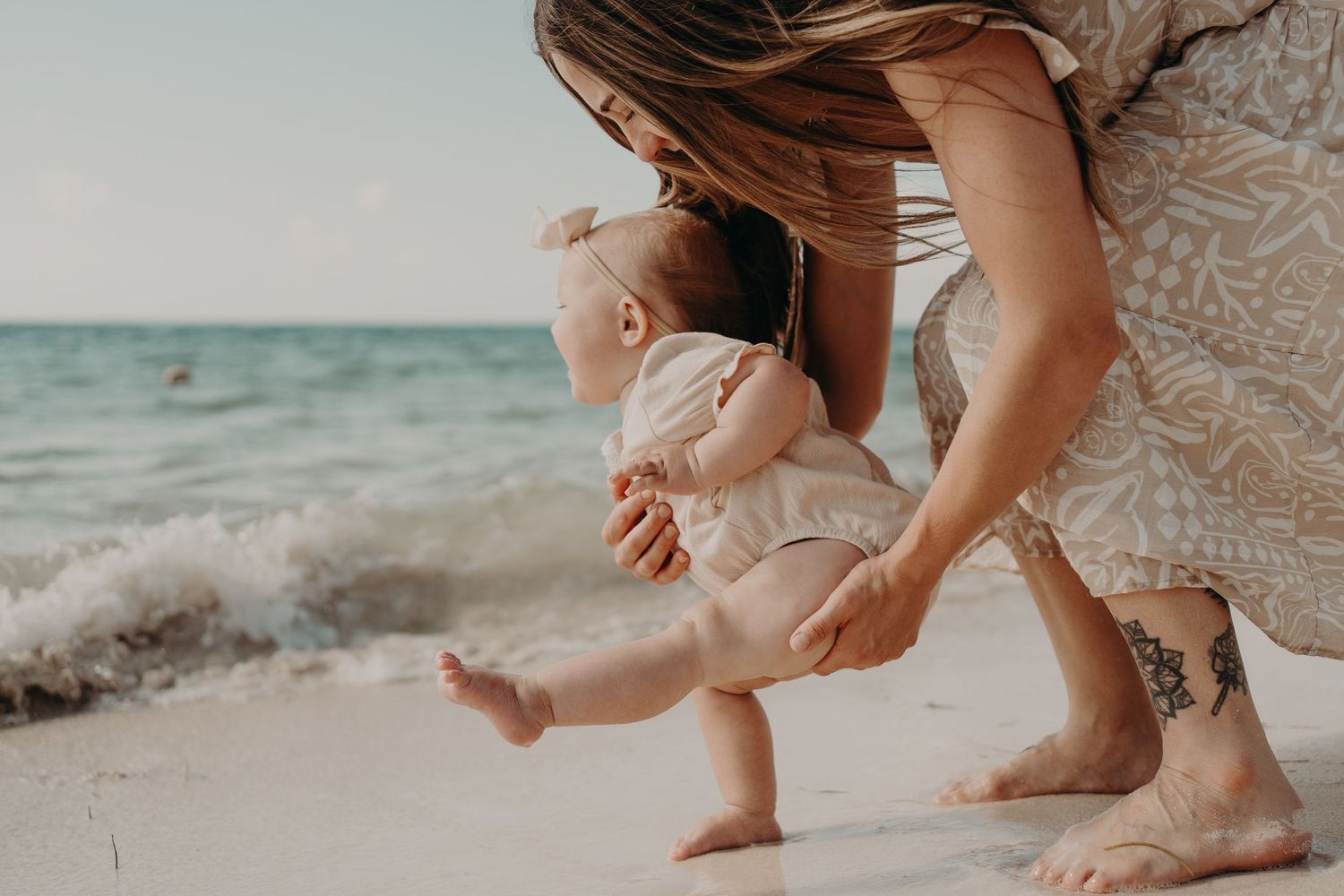 A tender moment between parent and child embracing on a sunny beach with soft pastel tones. Family photography Puerto Morelos.