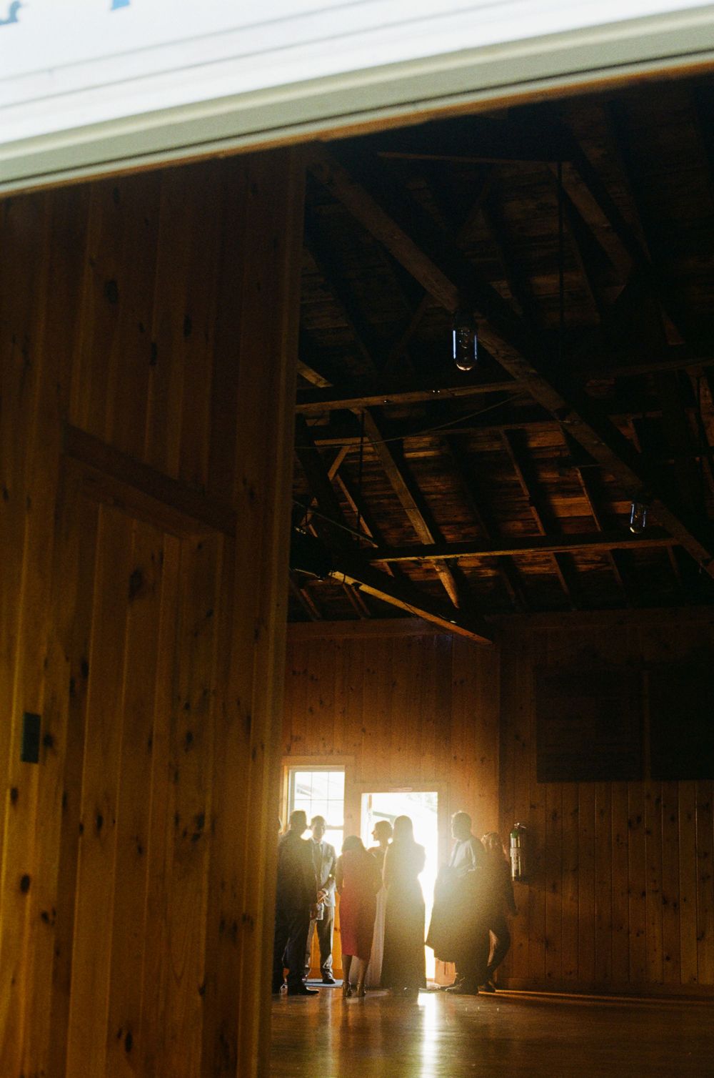 The wedding party gathers before the ceremony and glows through the light by the door, the summer sun illuminates their dresses and joy.