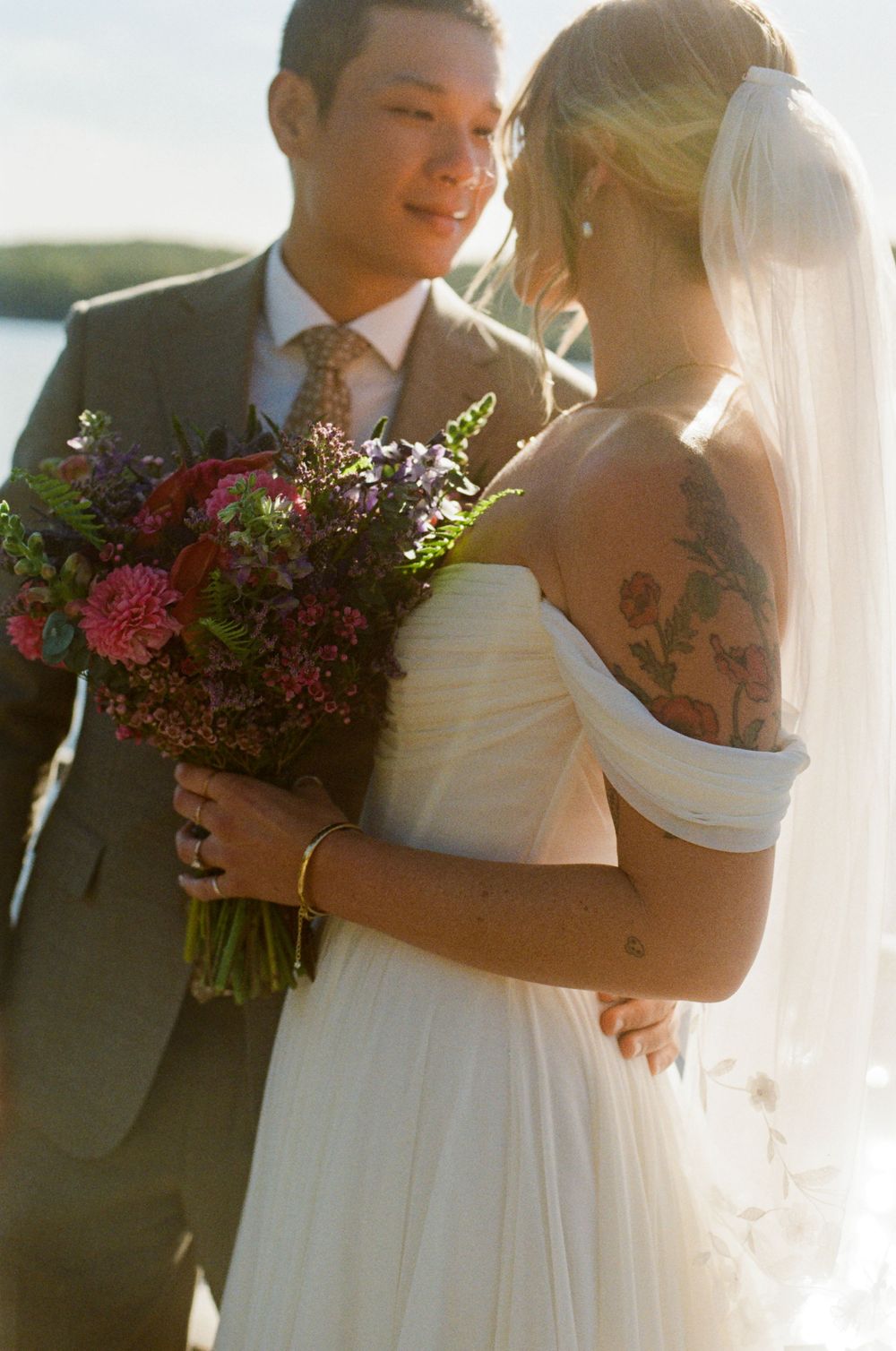 The bride looks at the groom as he looks back at her, both glowing in love and sunlight on a summers day at Kamp Kohut in southern Maine.