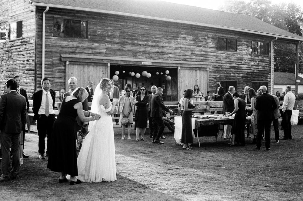 Wide shot of the mother of the bride bustling her dress while guests enjoy homemade food and the reception decorations in southern Maine.