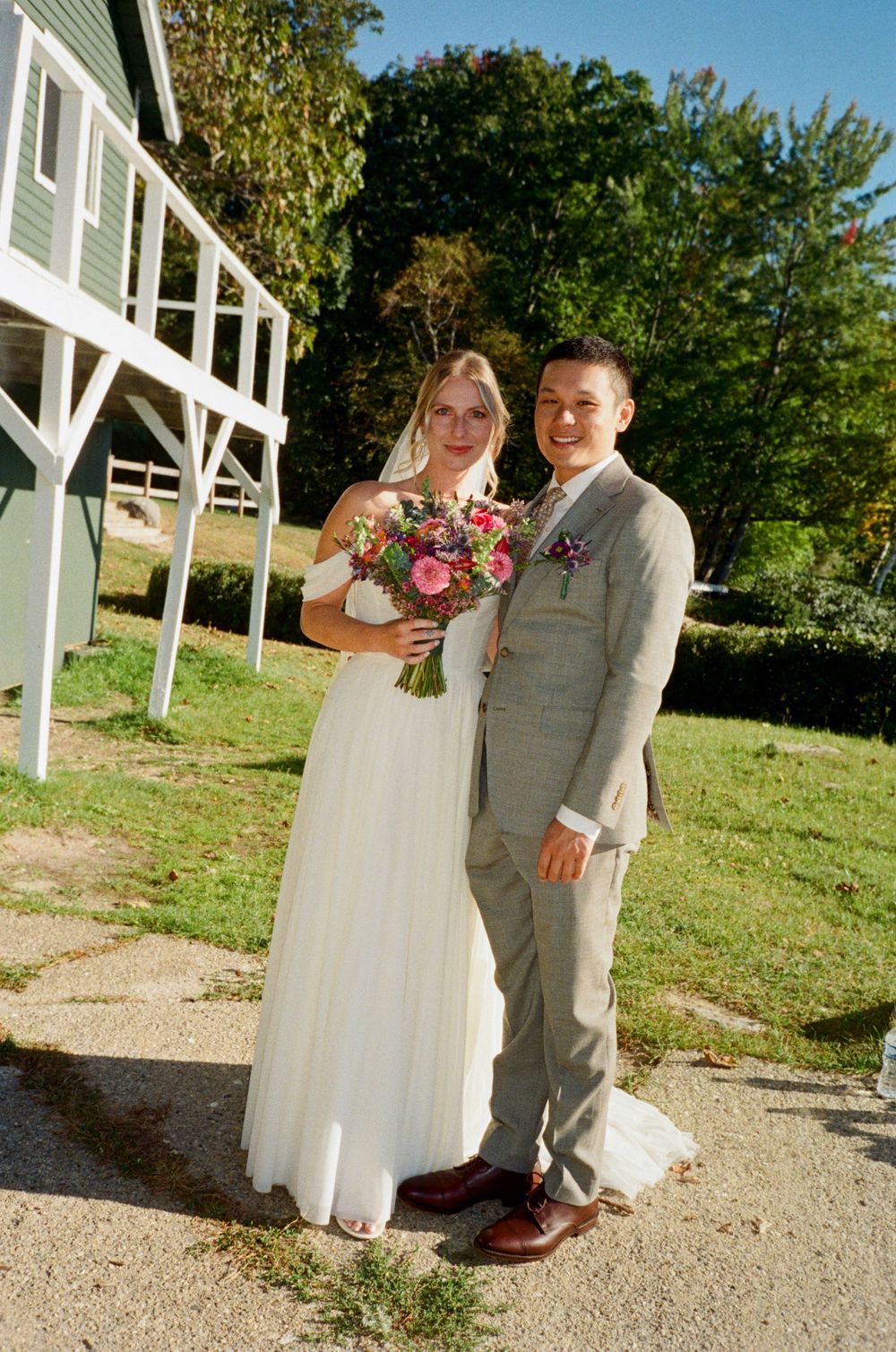 Portrait of the wedding couple outside before getting married. She holds her colorful bouquet, he holds onto her smiling together in Maine.