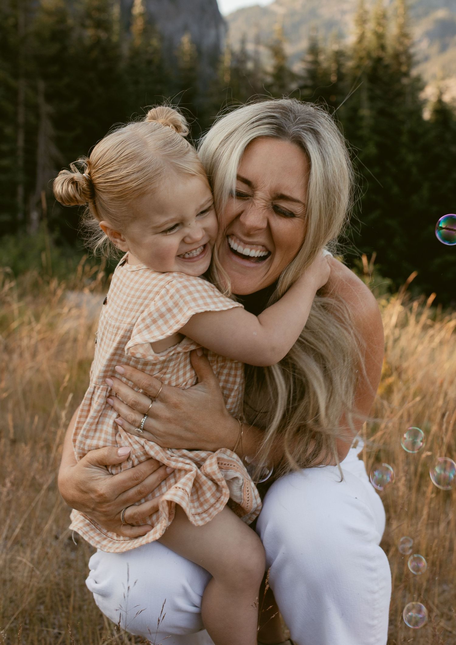 A couple shares a joyful moment together in a mountainous forest setting during golden hour.
