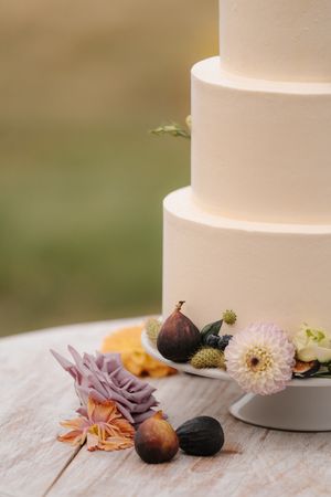 Close-up detail of a white tiered wedding cake decorated with fresh figs and pastel flowers.