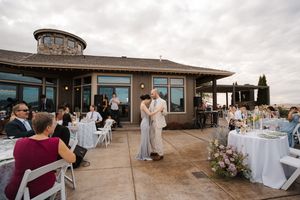 Panoramic view of a coastal wedding reception venue with guests mingling on an outdoor terrace.