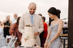 A couple cuts their elegant white wedding cake at an outdoor reception.