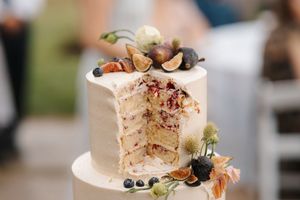 A white wedding cake decorated with fresh berries, figs, and nuts sits elegantly on display.