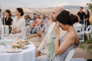Wedding guests seated at outdoor reception tables enjoy food and conversation at sunset.