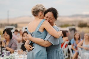 Two guests share an emotional embrace during an outdoor reception with desert mountains in the background.
