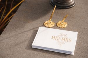 Gold wedding earrings displayed next to a white Mr and Mrs card on a dark gray surface.