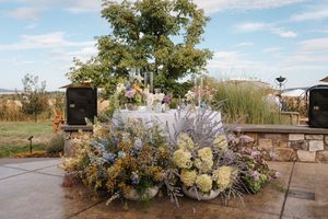 Elegant floral arrangements with white and blue blooms decorate a rustic outdoor wedding venue at sunset.