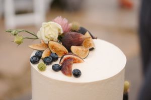 A white frosted cake decorated with fresh blueberries, figs, and delicate edible flowers on a rustic wooden surface.