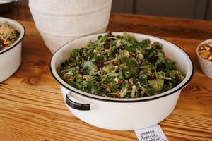Fresh salads and appetizers displayed in white bowls on a rustic wooden table at a catering event.