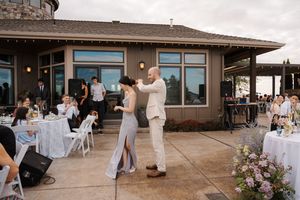 A panoramic view of a rustic wedding reception venue with white tables and chairs set up on a wooden deck.