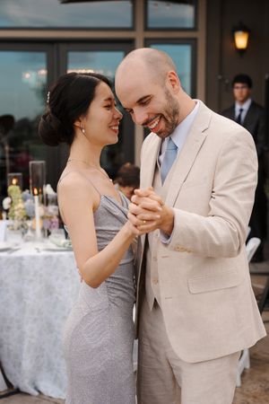 A couple in formal attire share an intimate dance moment at an outdoor wedding reception with elegant table settings.