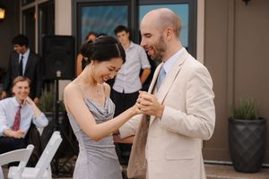 Two people share a joyful moment dancing together at an outdoor event, with guests seated in white chairs nearby.