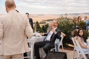 Wedding guests mingle and socialize during an outdoor reception with rolling hills in the background.