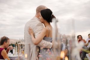 A couple embraces during their outdoor wedding reception at sunset with a city skyline in the background.