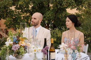Elegant outdoor wedding reception table settings with floral centerpieces and glassware under trees at dusk.