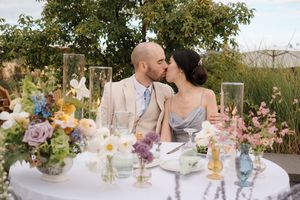 A couple shares a kiss at their garden reception table decorated with floral centerpieces and glowing candles.