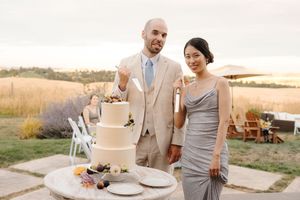 Wedding reception setup with elegant white cake and table settings against a sunset backdrop.