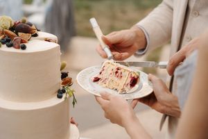 Hands delicately assemble and decorate a white wedding cake with floral details on a cake stand.