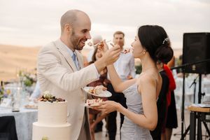 Couple sharing cake at their wedding reception with guests looking on and smiling.