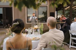 Wedding guests enjoy an outdoor reception celebration with string lights and natural decor at a rustic venue.