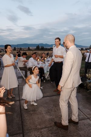 Couples in white and beige attire dance together at an outdoor reception during sunset.