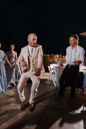 Wedding guests in white attire dance and celebrate on a dimly lit dance floor during an evening reception.