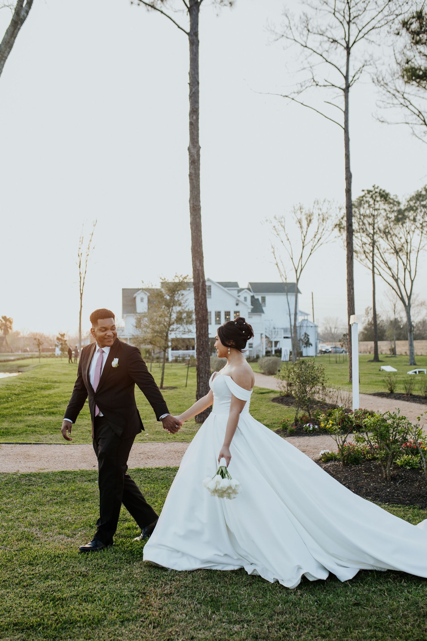 Wedding couple playfully interacts on grassy field with white dress flowing in the wind.