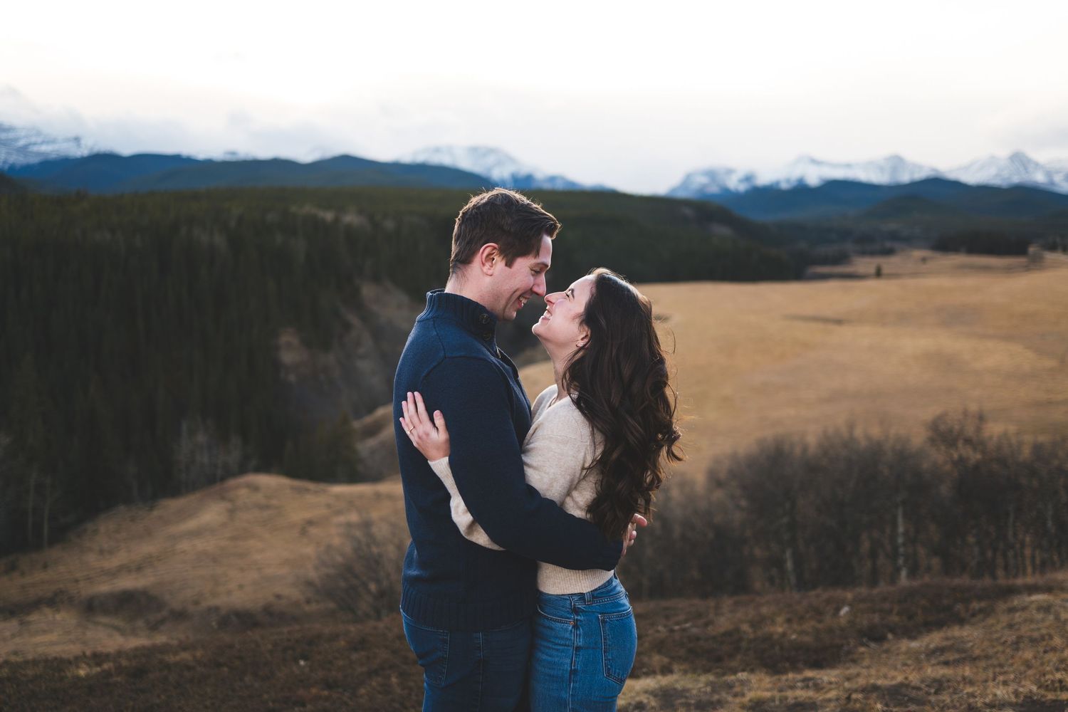 Romantic engagement photos in an open field with mountains in the distance.