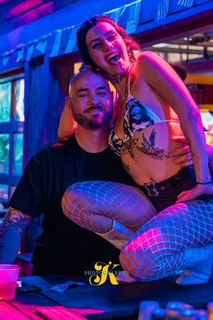 Intimate couple poses in vibrant neon lighting at a nightclub with pink and blue hues creating a moody atmosphere.