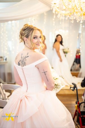 A person in a blush pink gown with a bow detail spins gracefully in an elegant room with crystal chandeliers.