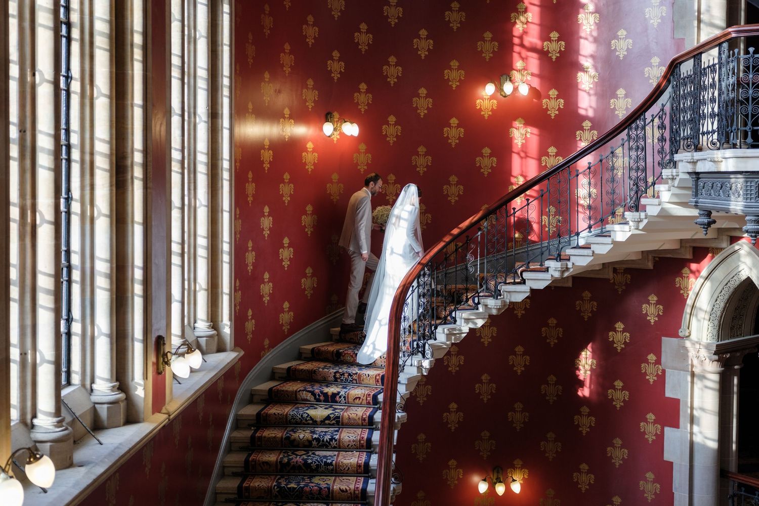 Ornate grand staircase in a historic mansion with red lighting and dramatic architectural details.