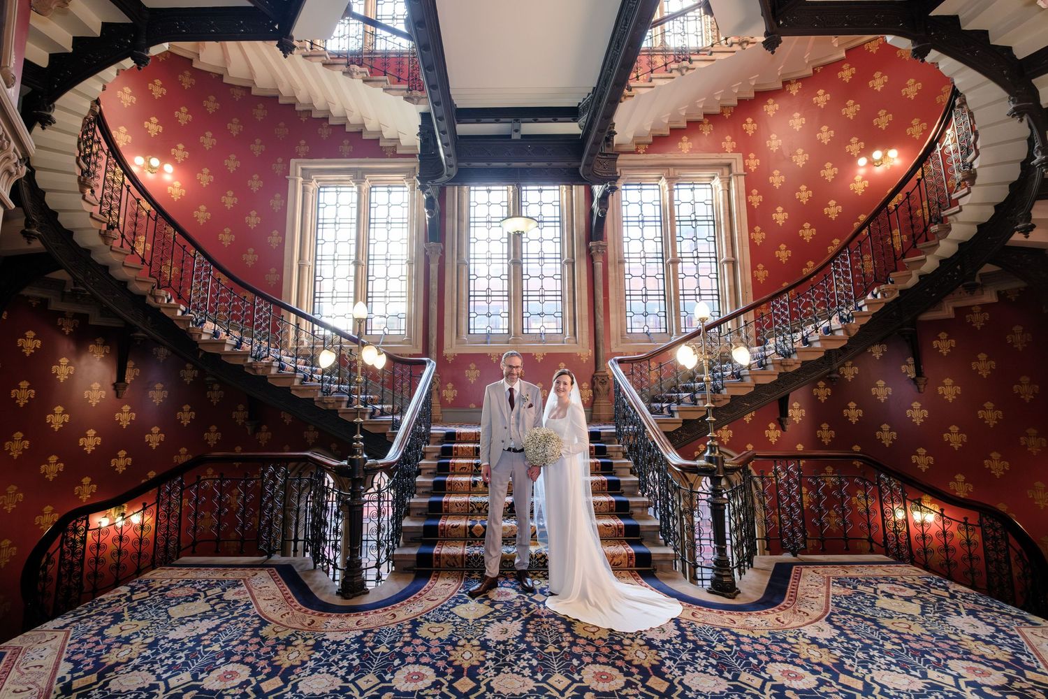 Ornate spiral staircase with red carpet and decorative railing in a historic building interior.