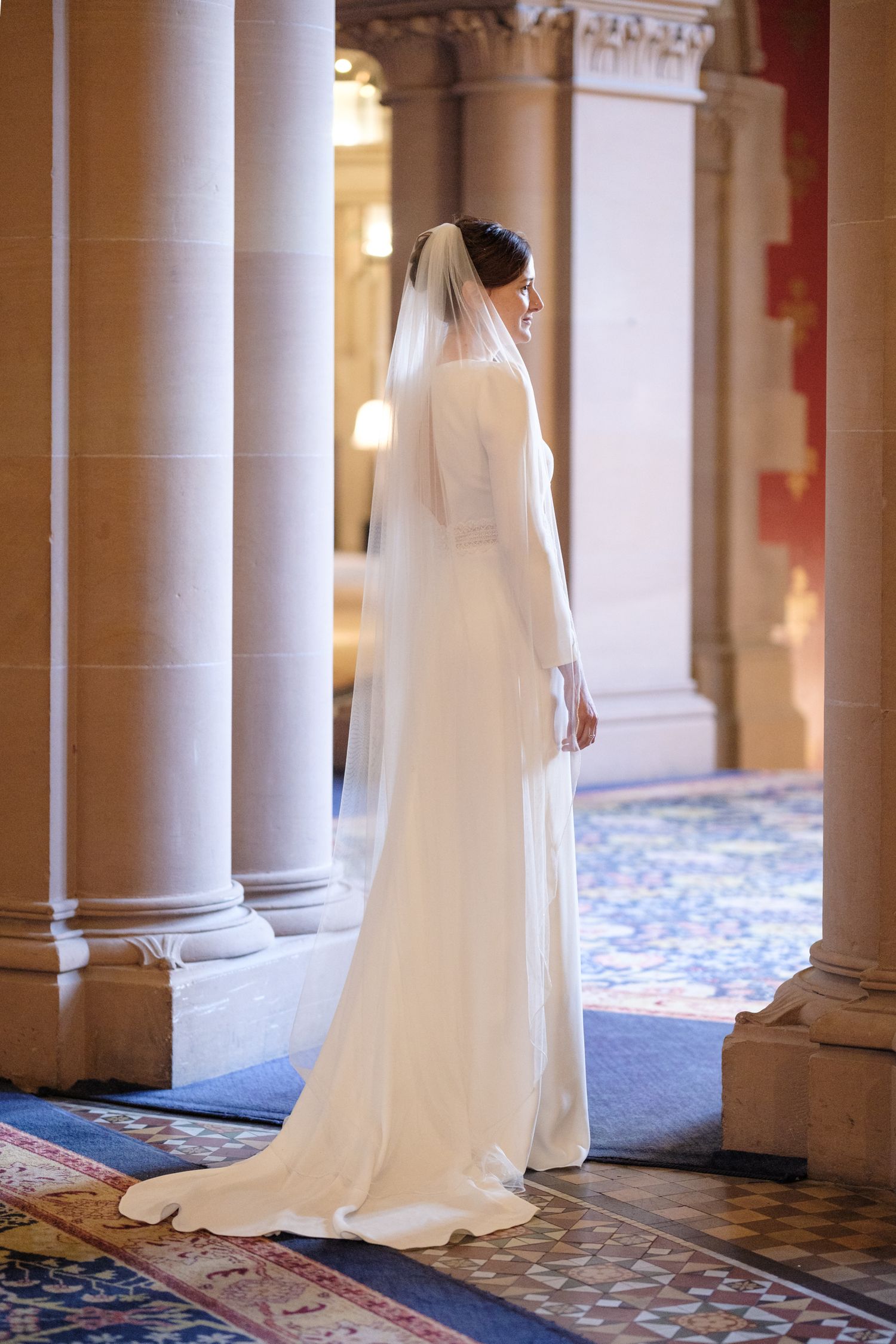 Elegant white wedding dress photographed in sequence along ornate colonnade with patterned carpet.