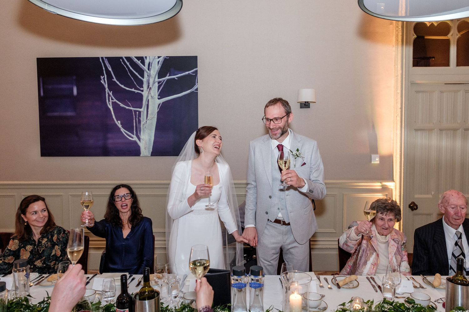 Wedding guests raise their glasses in a toast during an elegant indoor reception celebration.