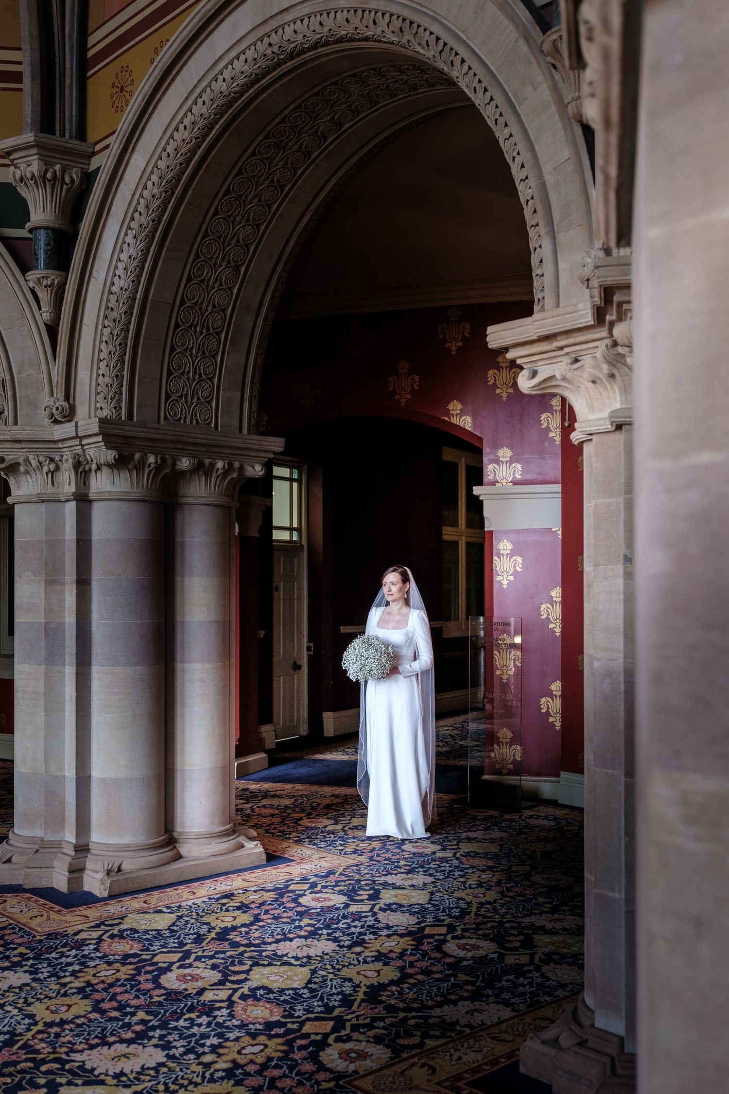 A ghostly figure in white stands in a grand hallway with ornate arches and blue patterned carpet.