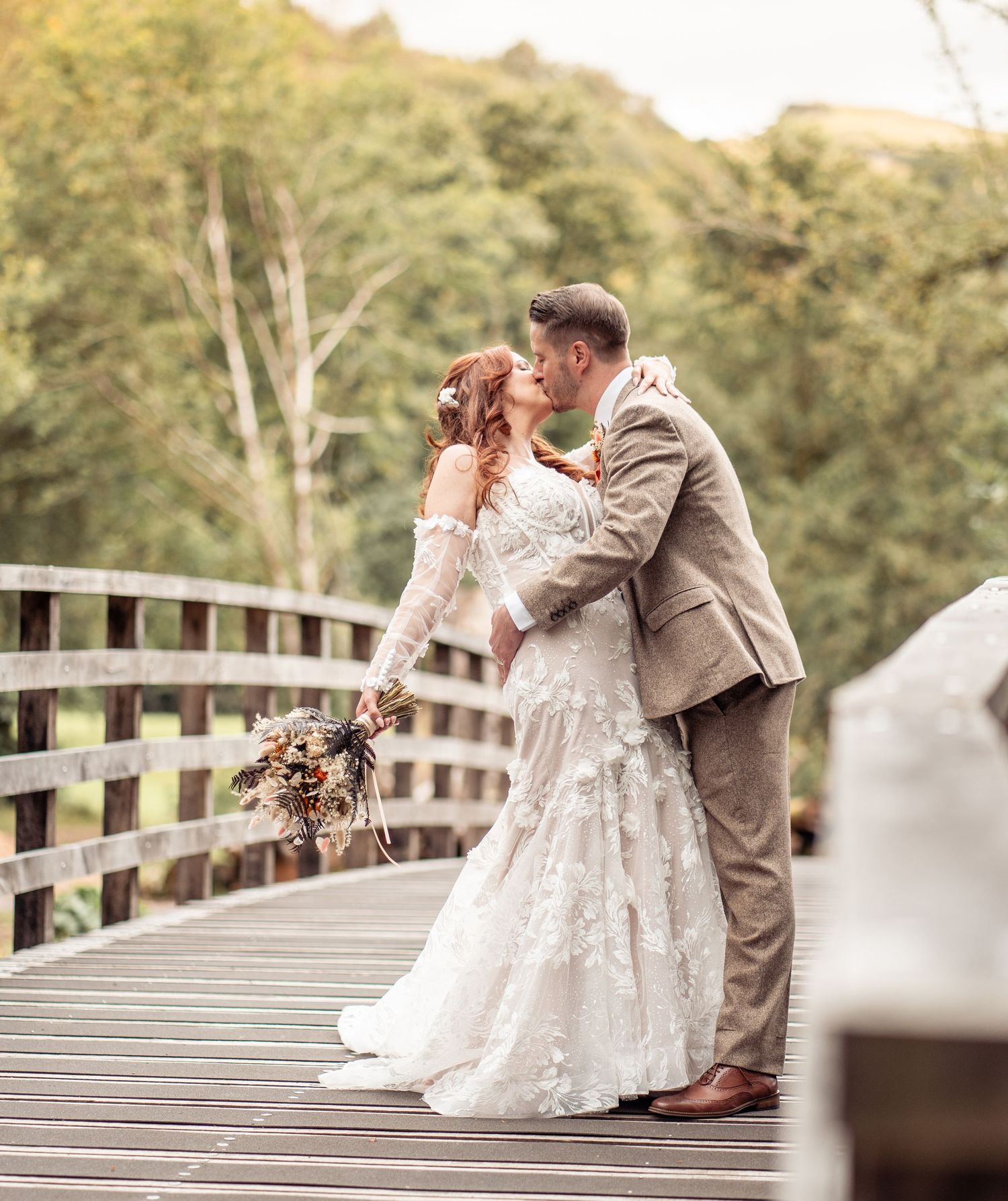A romantic wedding couple shares an intimate moment on a wooden bridge surrounded by autumn foliage.