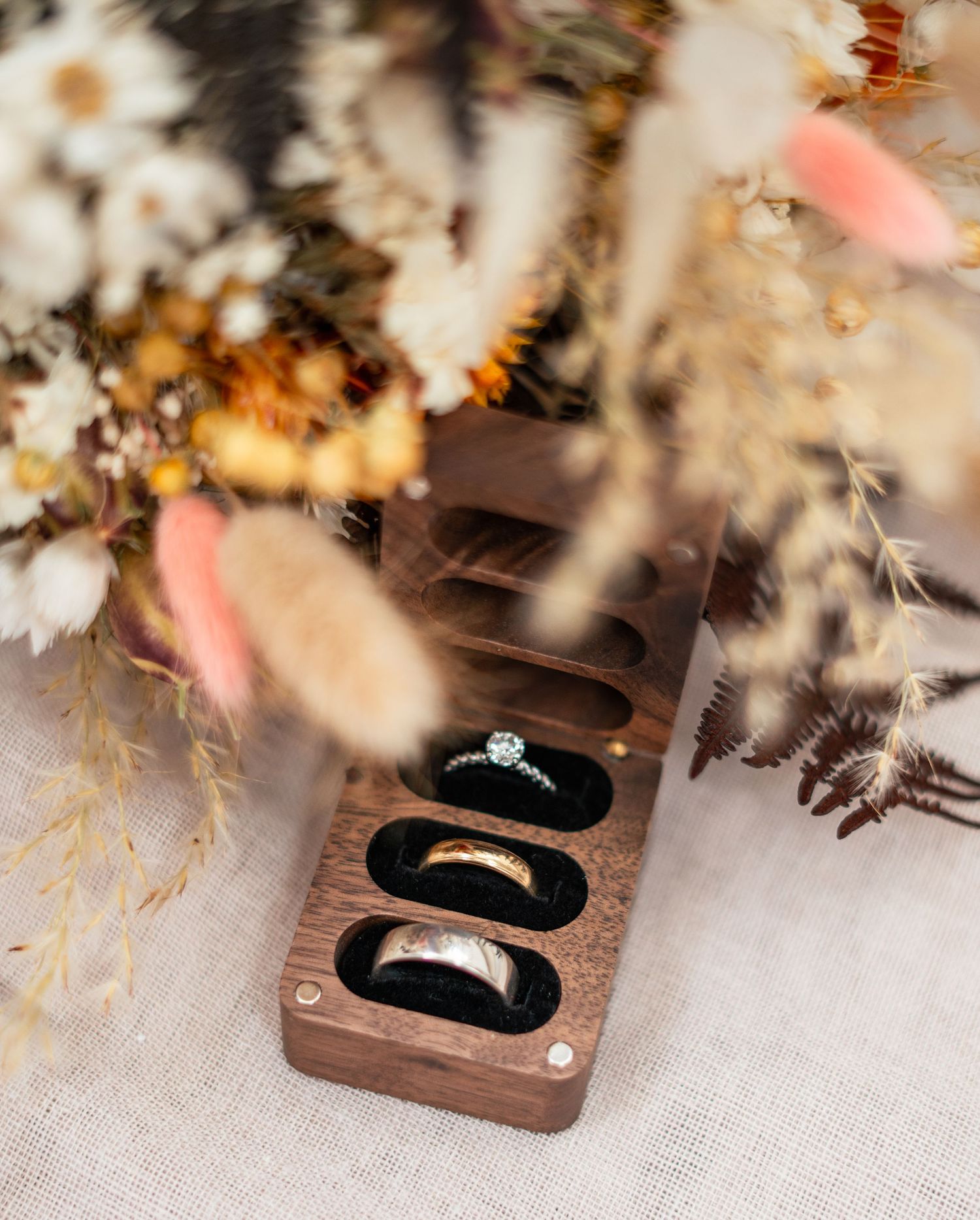 Two wooden ring boxes with white feather decorations and soft pink accents displayed on a light fabric surface.