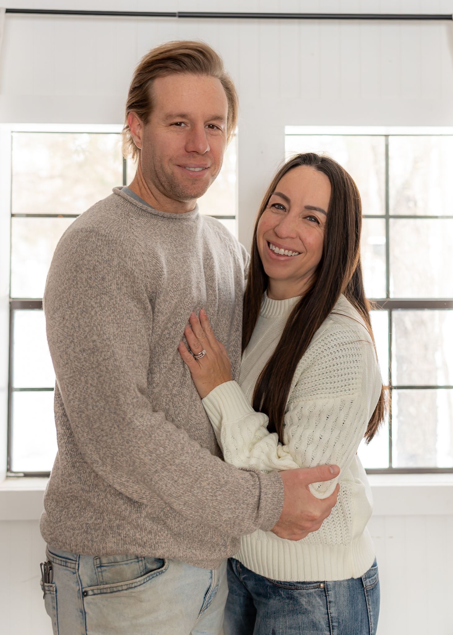Couple in cozy sweaters embracing in bright modern room with natural light.