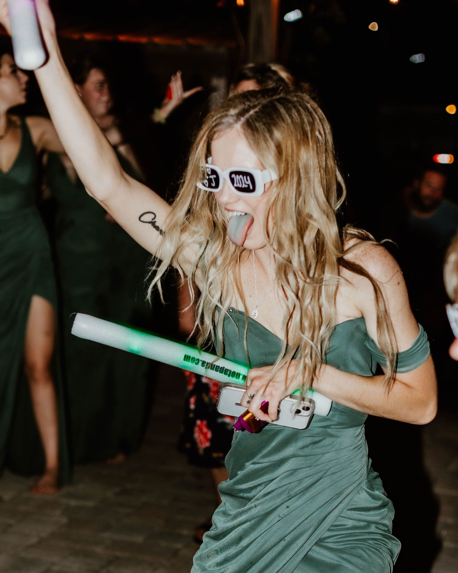 Group wearing green outfits dancing and holding light sticks at a nighttime party celebration.