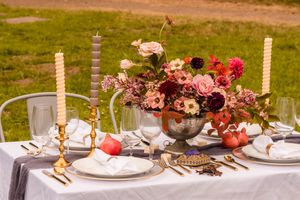 An elegant outdoor table setting with pink floral centerpieces, gold candlesticks, and white plates arranged on a long table in northern ca